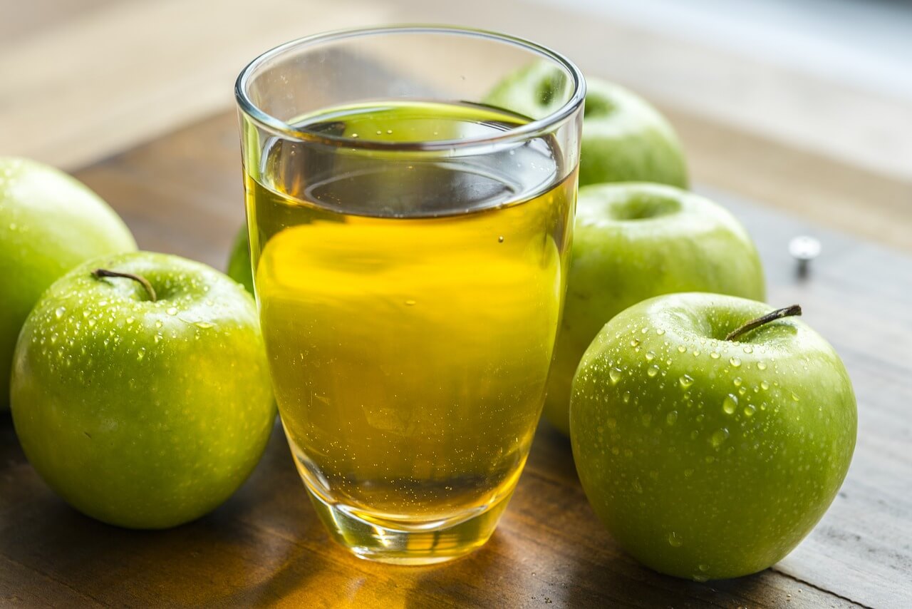 Larutan cuka apel dalam gelas kaca, dikelilingi buah apel hijau